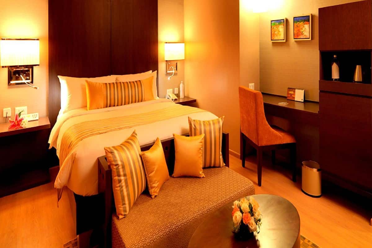 A hotel room with a large bed, bedside lamps, a desk, a chair, and a small table with flowers.
