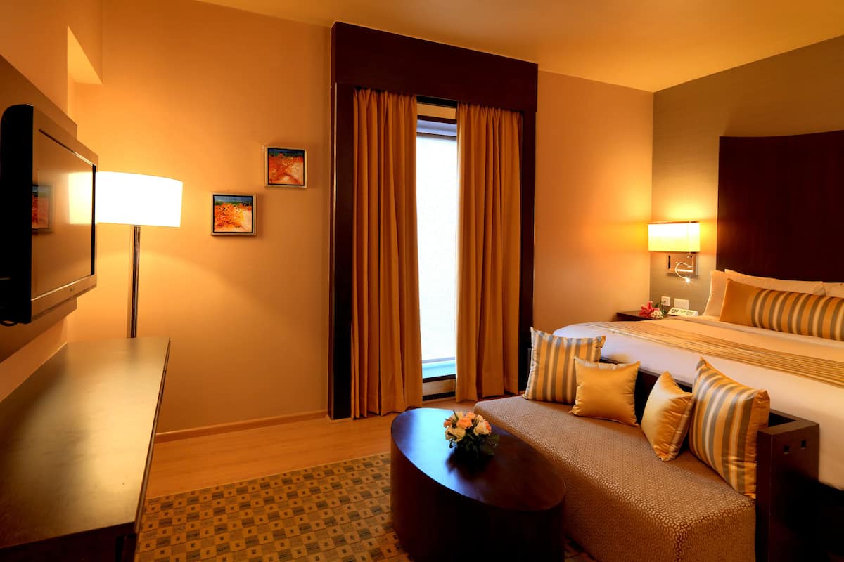 A hotel room with a bed, bedside tables, a desk, a lamp, and a window with curtains.