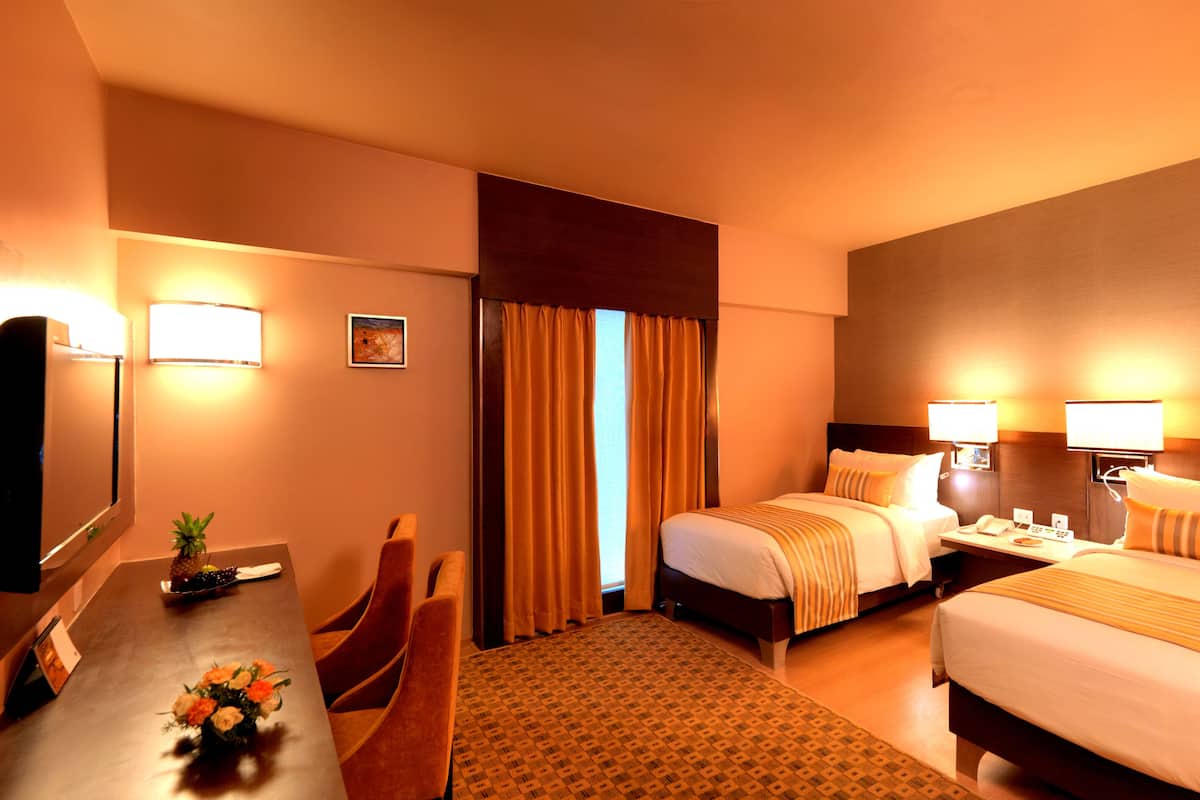 A hotel room with two beds, a desk with a chair, a TV, and a painting on the wall.