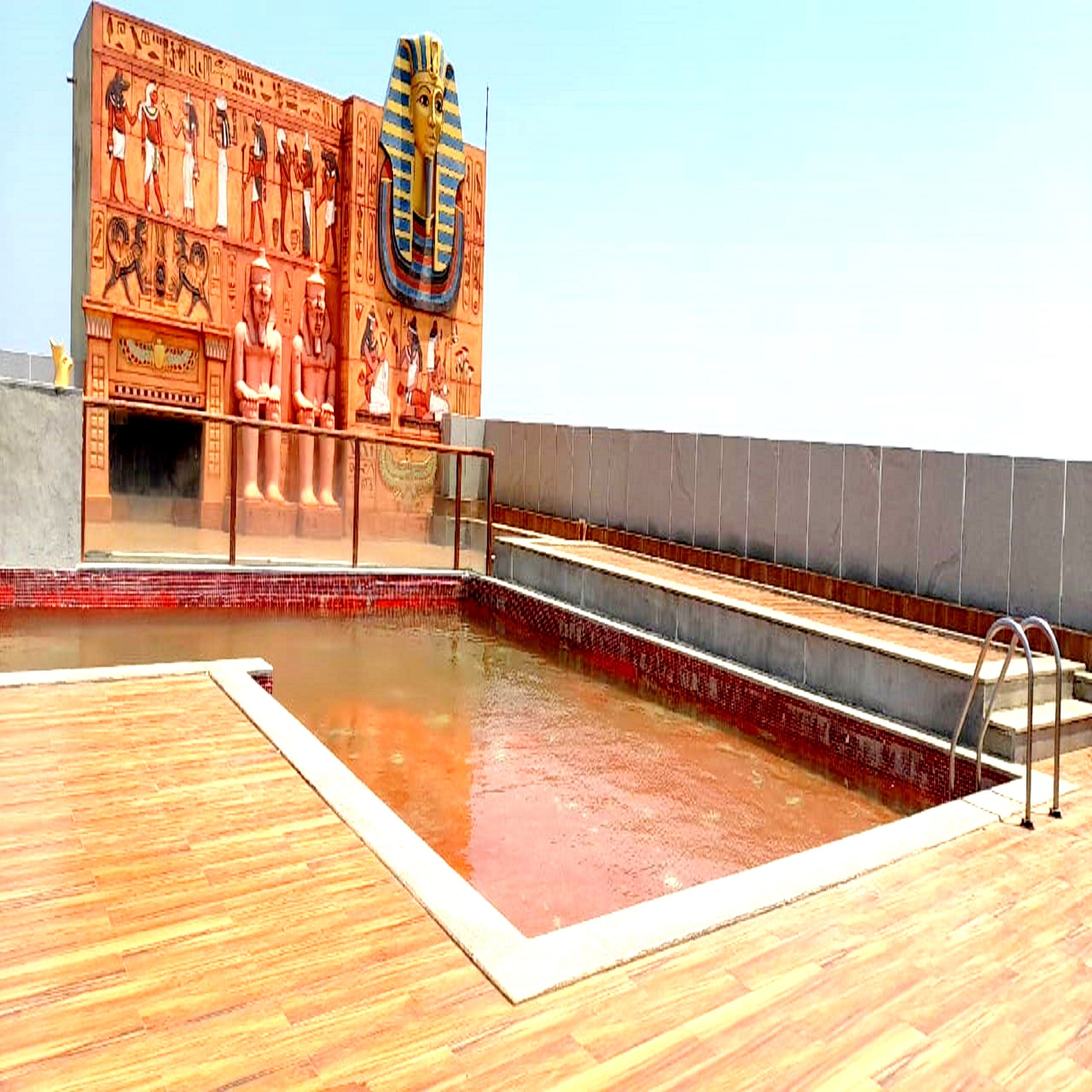 A swimming pool with a wooden deck and a wall with ancient Egyptian hieroglyphs.