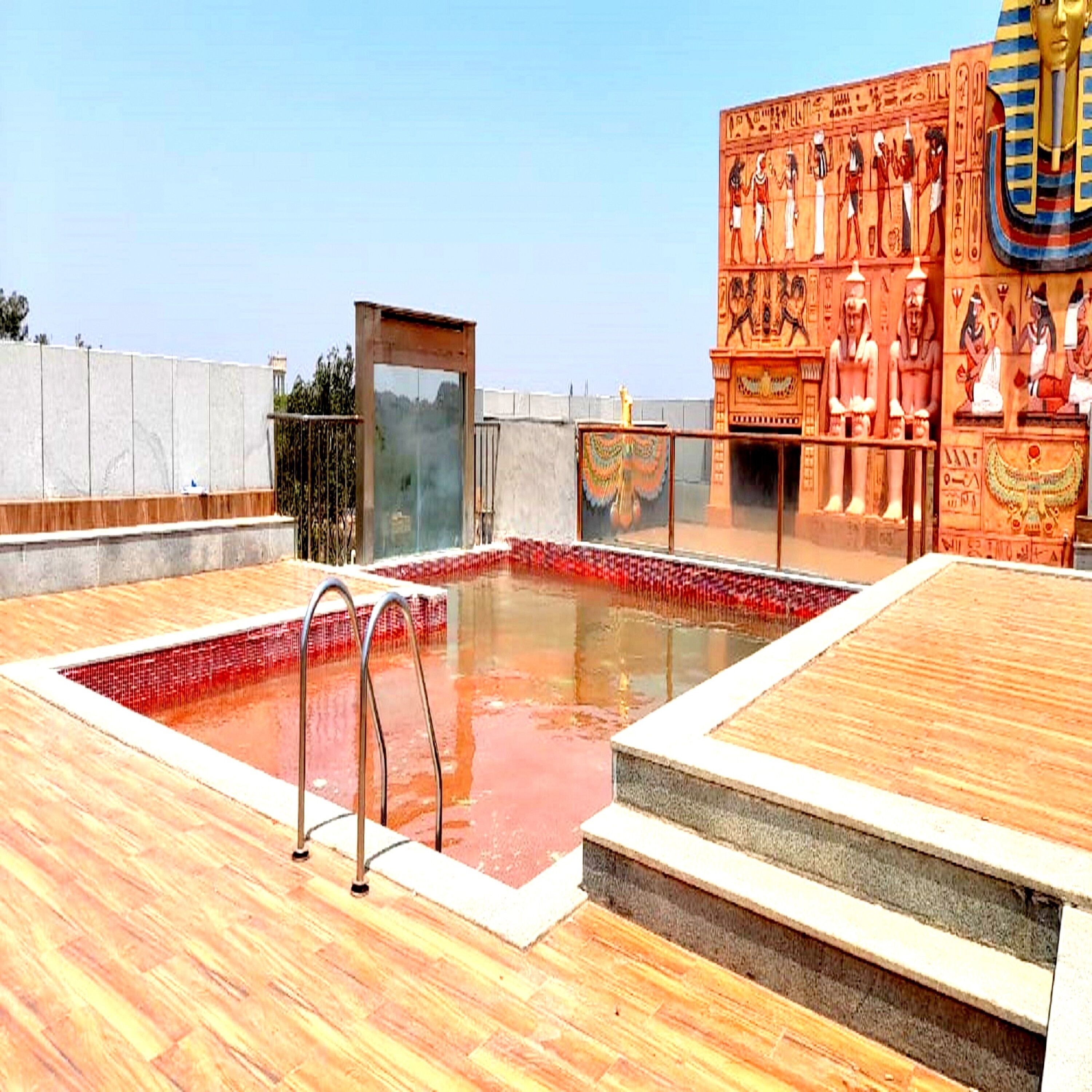 A swimming pool with a wooden deck and a wall with ancient Egyptian carvings.