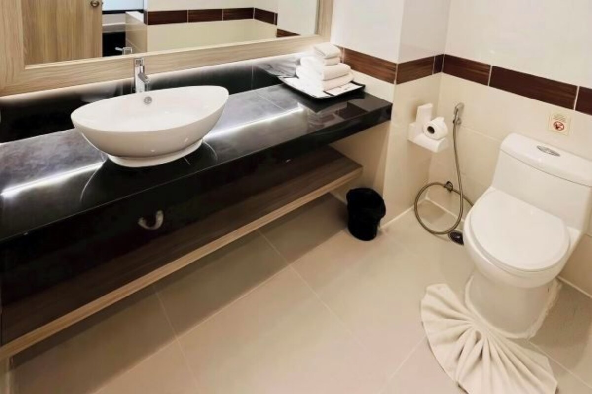 Un baño moderno con un lavamanos grande de color blanco, encimera negra y un inodoro con cubierta decorativa.