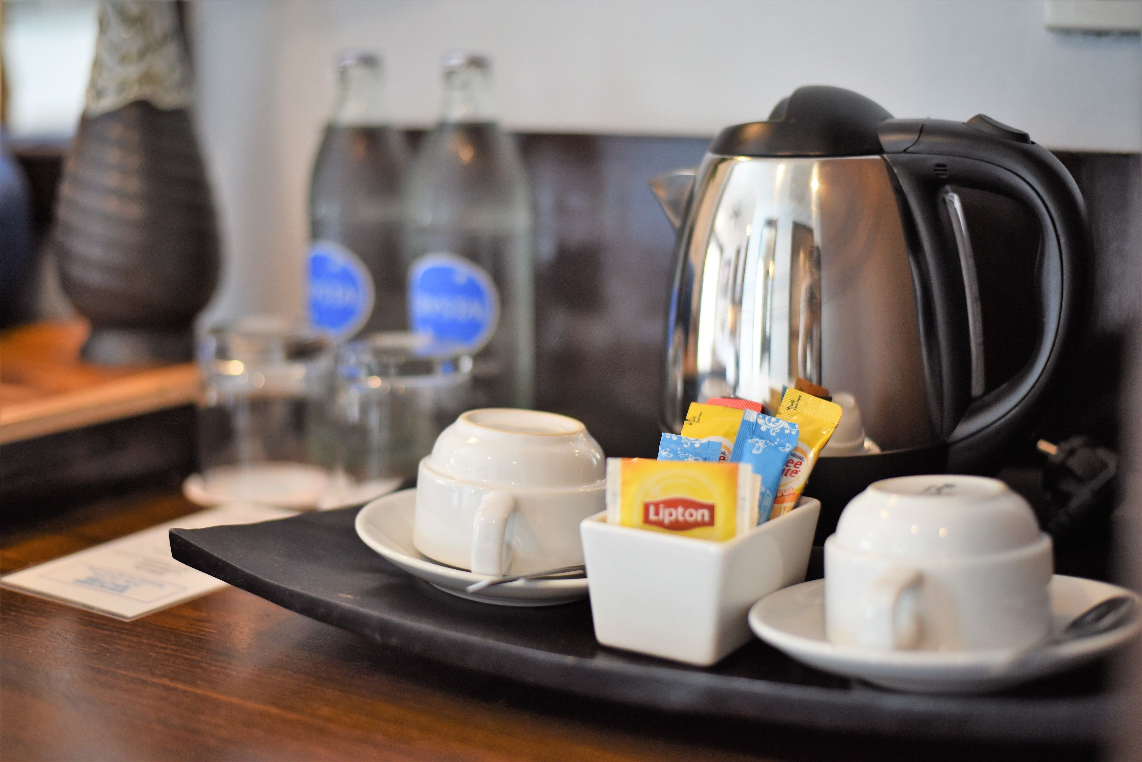 A coffee station with two cups, a teapot, and Lipton tea packets.