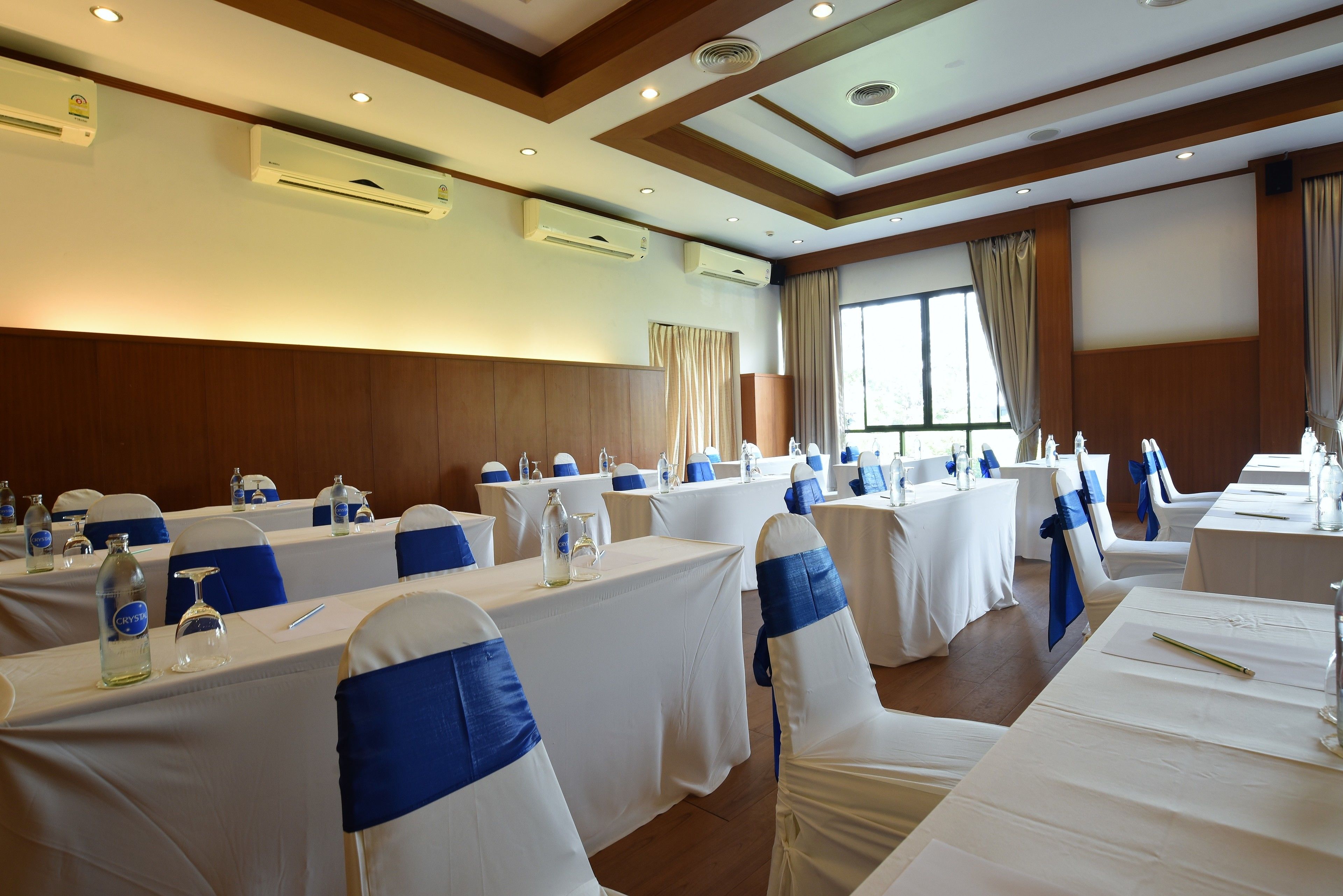 A conference room with multiple tables, white tablecloths, and blue sashes on chairs.