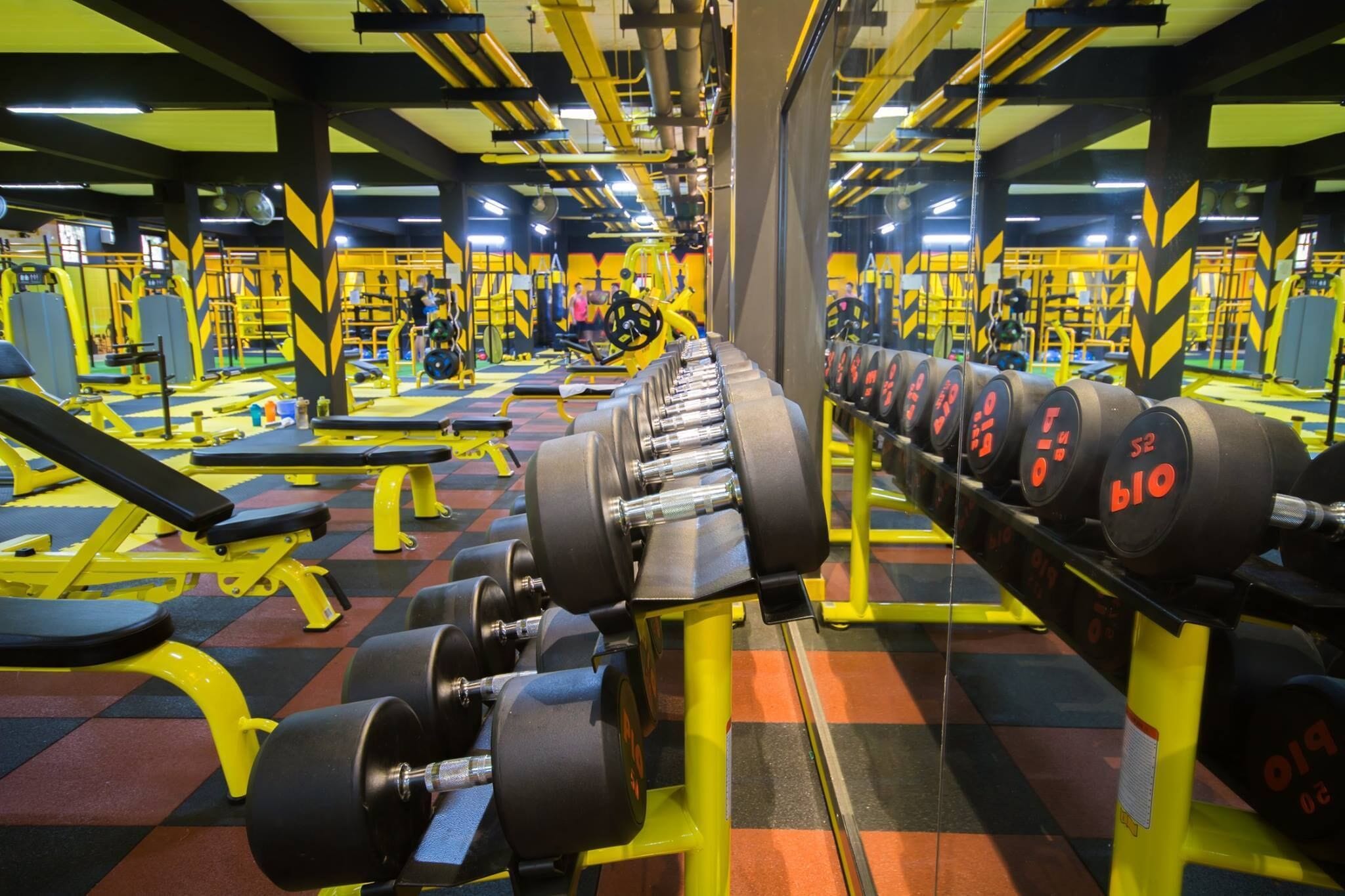 Een sportschool met gele apparatuur, zwart-gele vloer en spiegels aan de wanden.