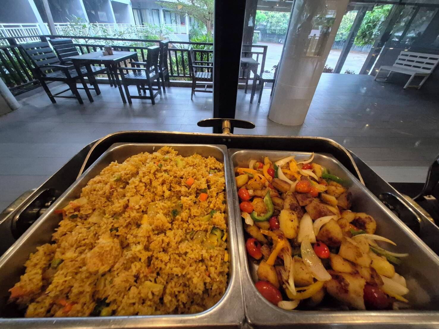 Un buffet con due vassoi di cibo: uno con riso e verdure, l'altro con patate e peperoni.
