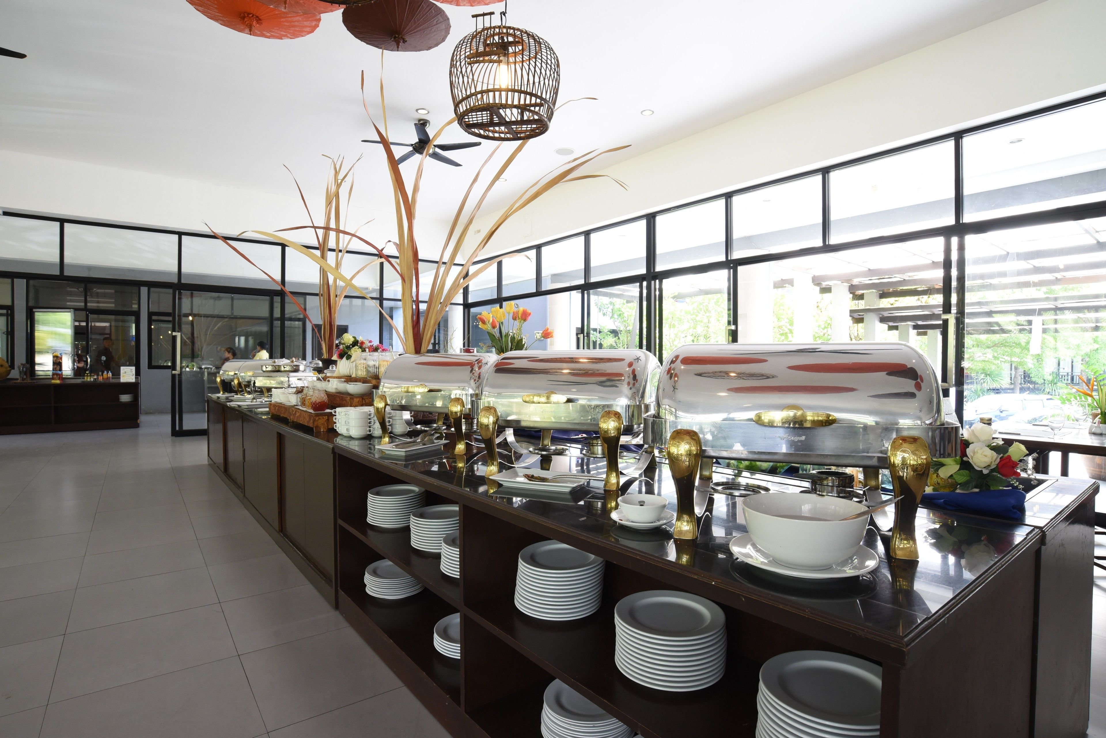 Un dispositiu de buffet amb diverses zones de servei, una gran varietat de plats i elements decoratius com plantes altes i un llum penjant.