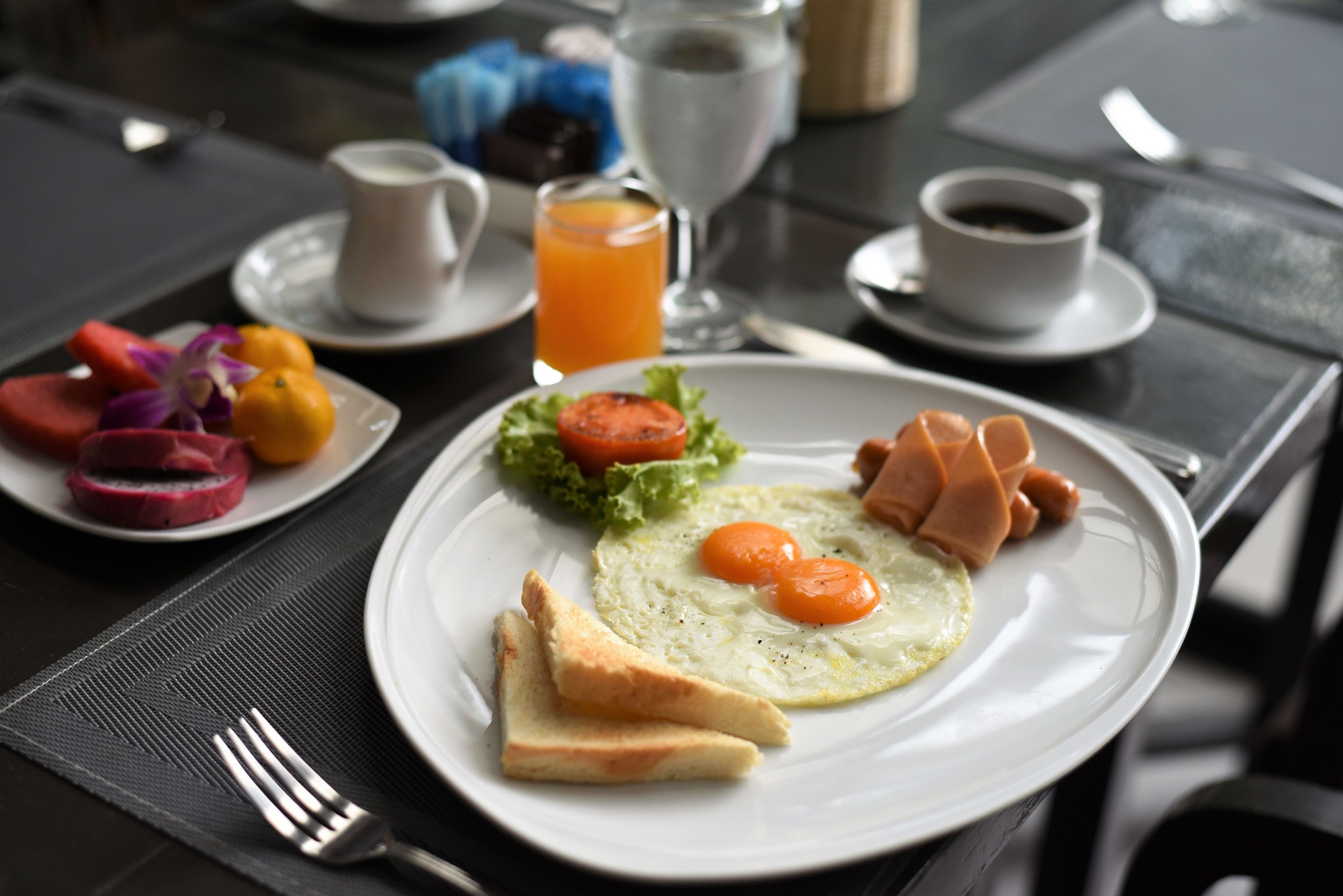 A breakfast setting with a plate of eggs, toast, and vegetables, along with a glass of orange juice and a cup of coffee.