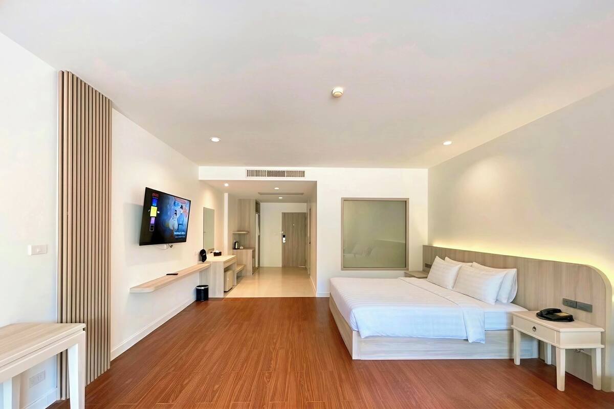 Una habitación de hotel moderna con una cama grande, mesitas de noche, un televisor y un vestidor.
