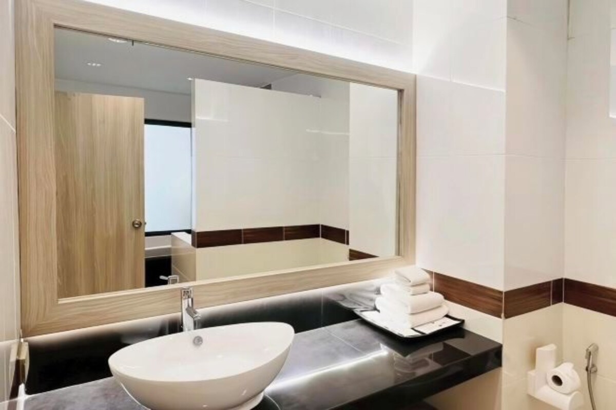 A modern bathroom with a large mirror, a white sink, and a black countertop.