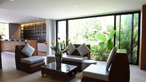 Un salon moderne avec un canapé, des fauteuils et une table basse. Une grande fenêtre offre une vue sur la verdure à l’extérieur.