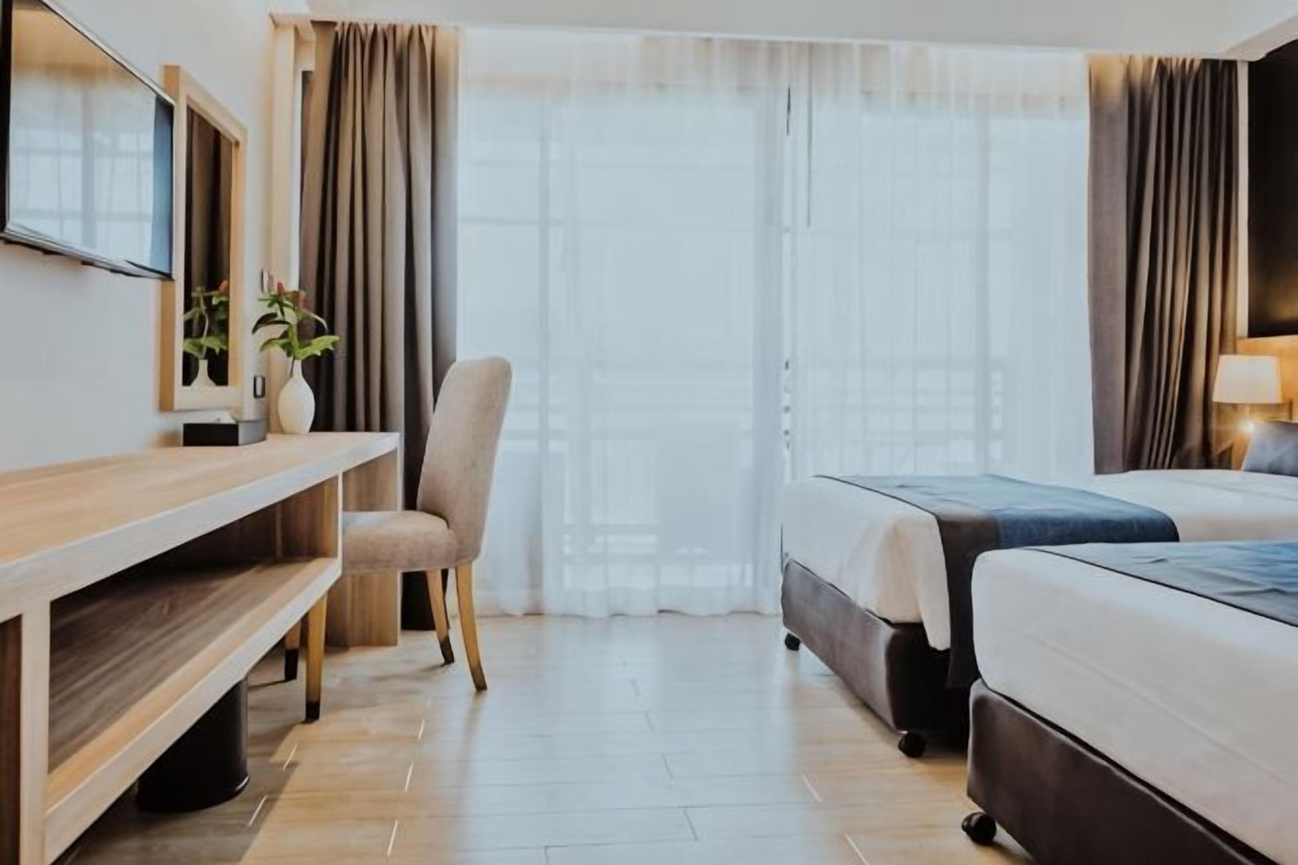 A hotel room with a bed, a desk, a chair, a TV, and a window with curtains.