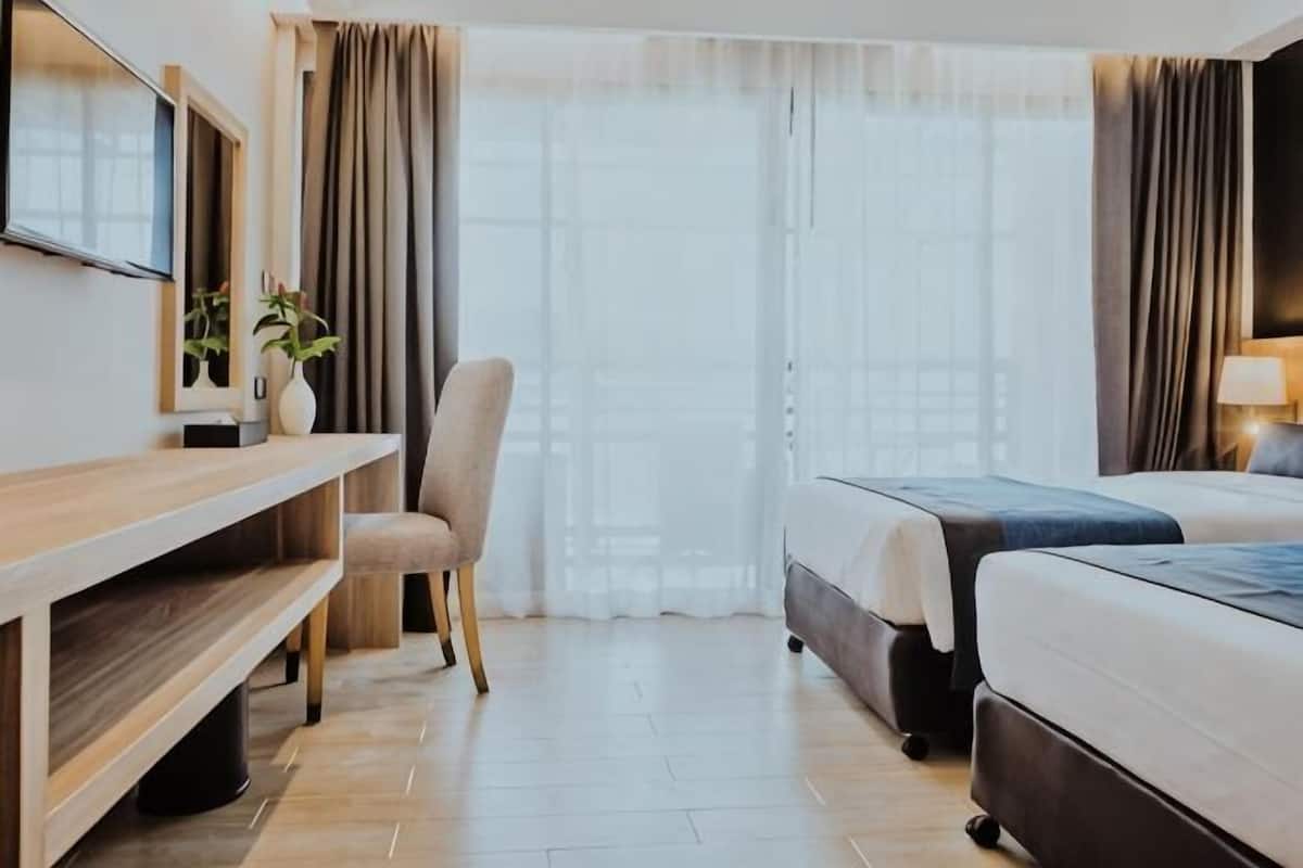 A hotel room with a bed, a desk, a chair, a TV, and a window with curtains.