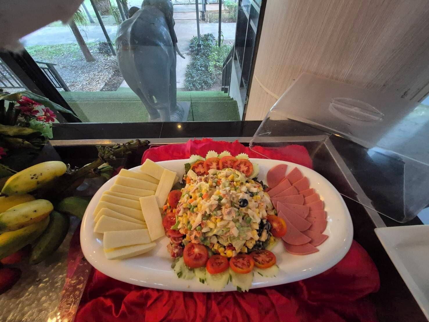 A buffet with various food items including sliced cheese, a salad with tomatoes and cucumbers, and sliced ham.