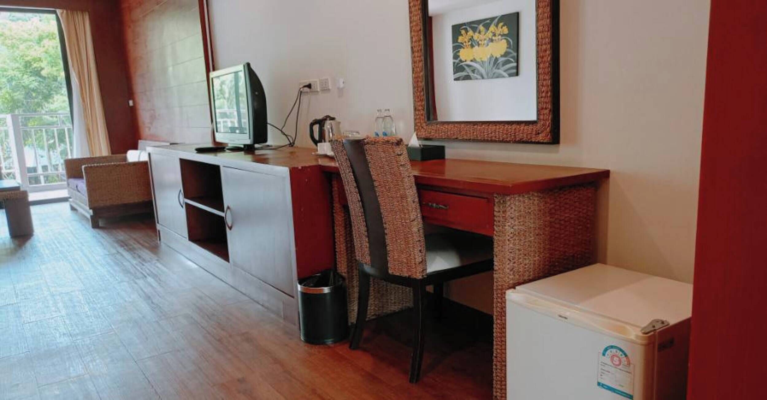 A compact room with a kitchenette, a desk with a chair, a television, and a small refrigerator.