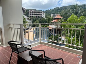 Un balcon donnant sur une piscine, un bâtiment doté d’un toit traditionnel et une colline verdoyante.