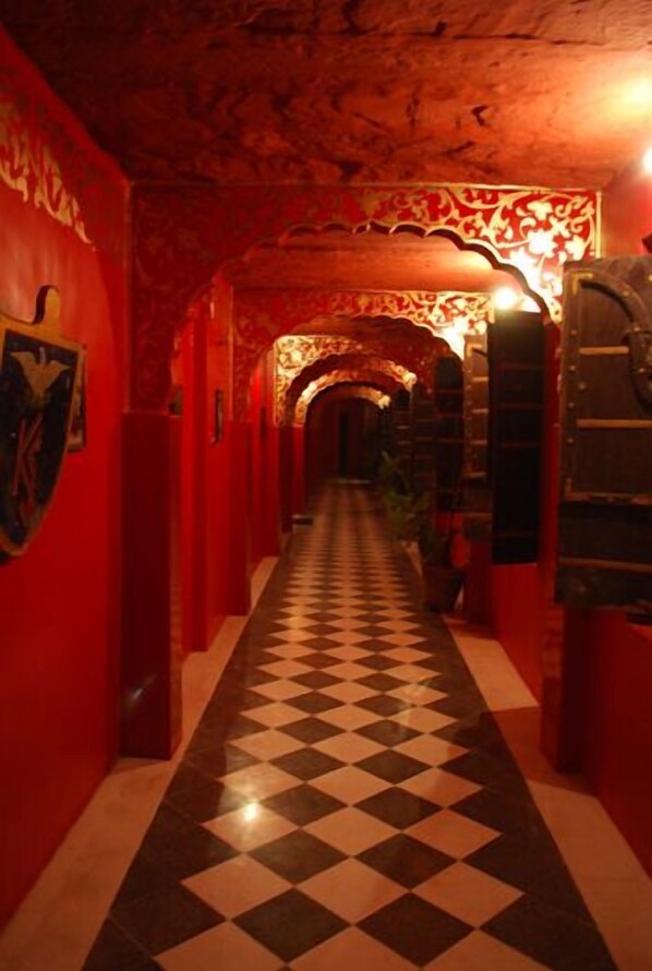 Un couloir aux murs rouges, au sol à carreaux noirs et blancs, et au plafond orné de motifs décoratifs.