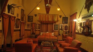 A room with a bed, two armchairs, a small table, and a patterned rug. - Hotel Bhairon Vilas (Bikaner)