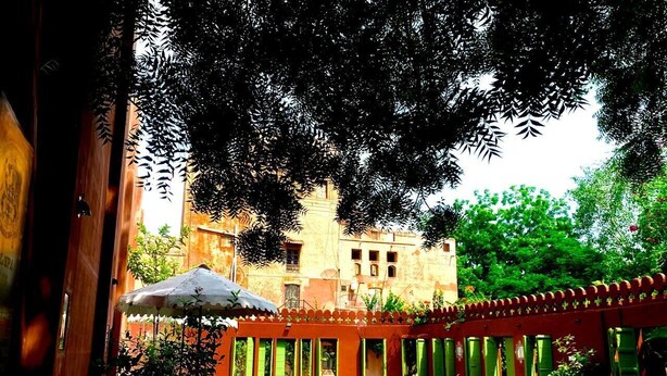 A swimming pool surrounded by a red fence, with a building in the background. - Hotel Bhairon Vilas (Bikaner)