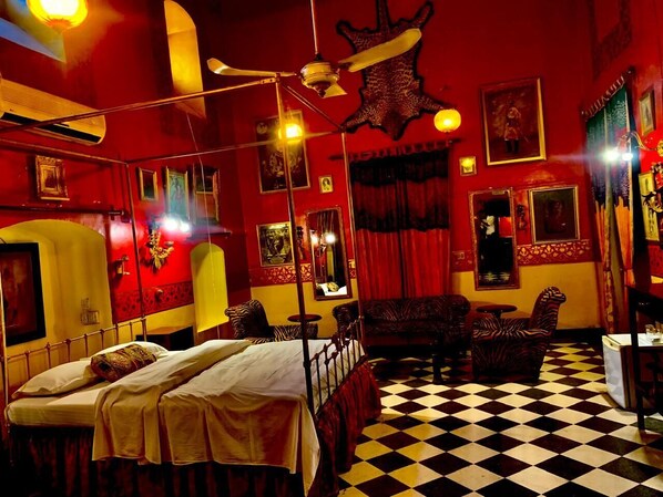 A room with a checkered floor, a bed with a canopy, a zebra-patterned armchair, and a mirror on the wall. - Hotel Bhairon Vilas (Bikaner)
