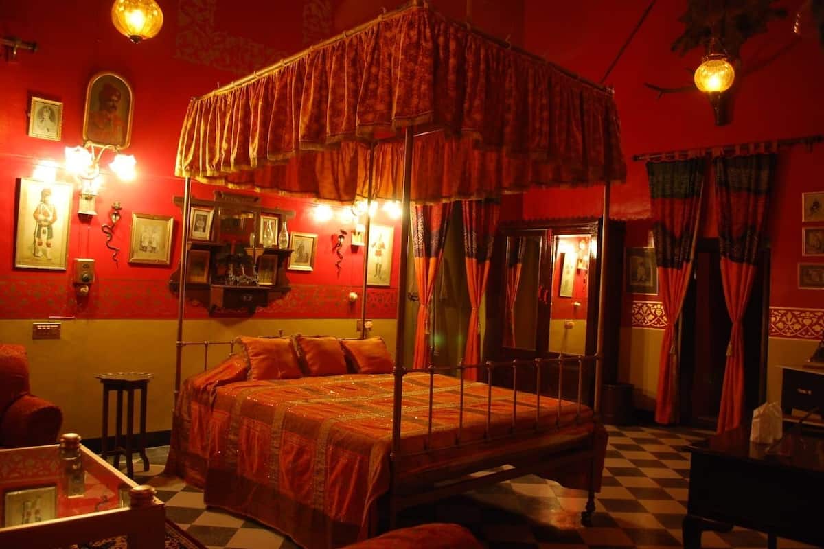 A traditional four-poster bed with a canopy, a checkered floor, and red walls with framed pictures.