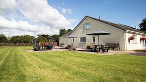 Een huis met een stenen gevel, een terras met tafels en banken, en een groot rond beeldhouwwerk.
