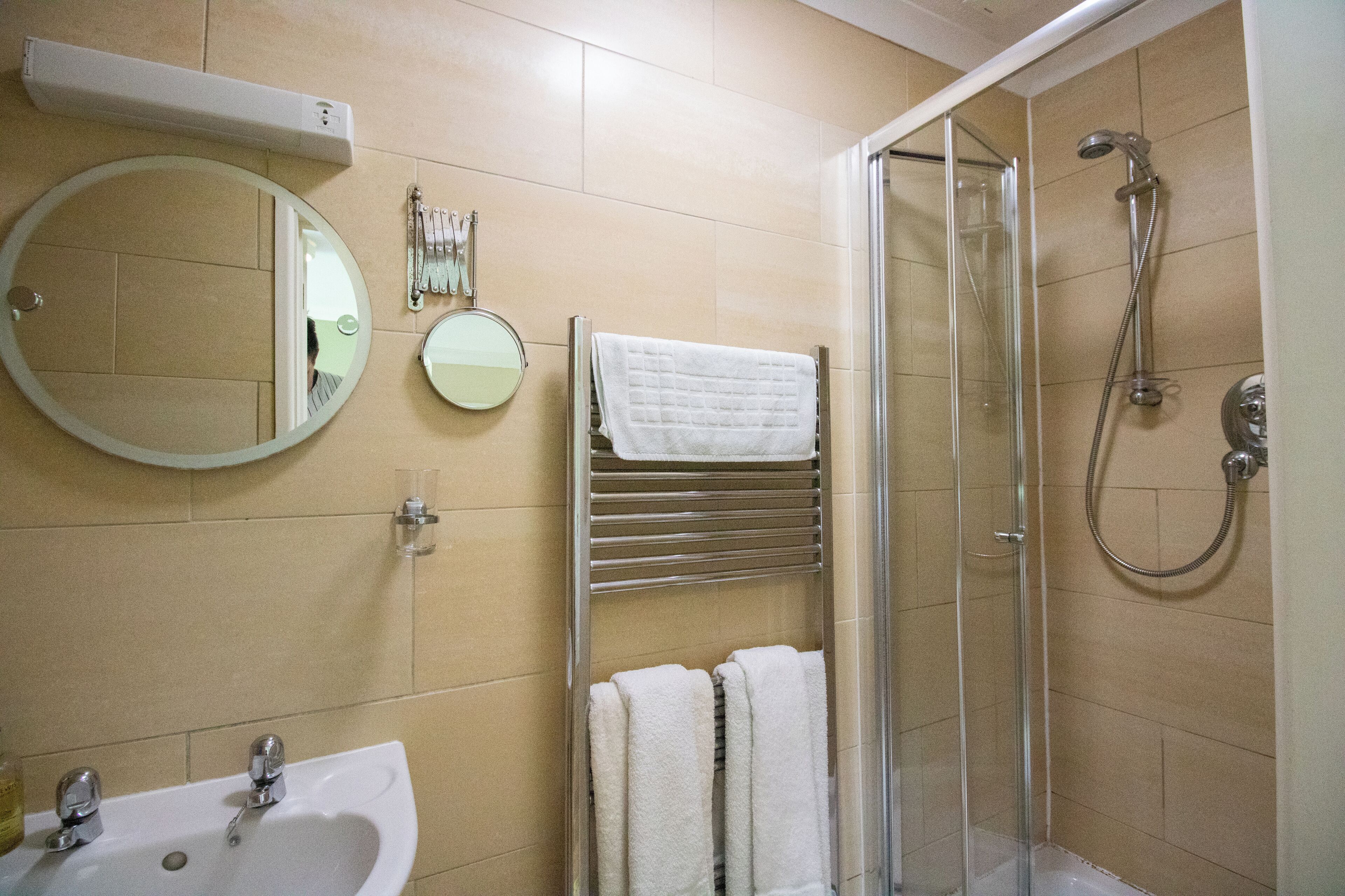 Un baño con lavamanos, espejo, toallero y ducha.