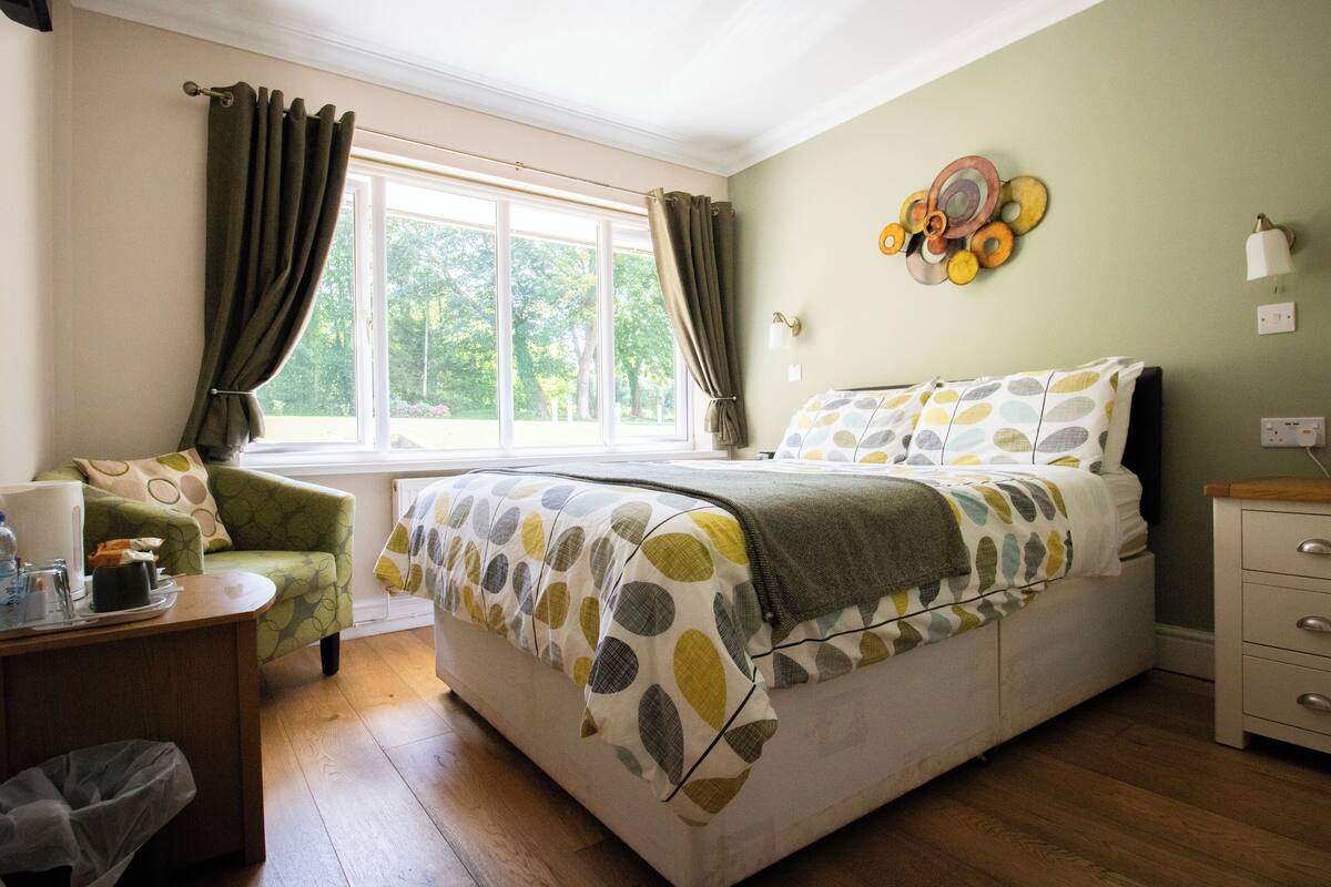 Une chambre à coucher comprenant un lit, une chaise, une table de chevet, une fenêtre avec des rideaux et un  élément de décoration murale.