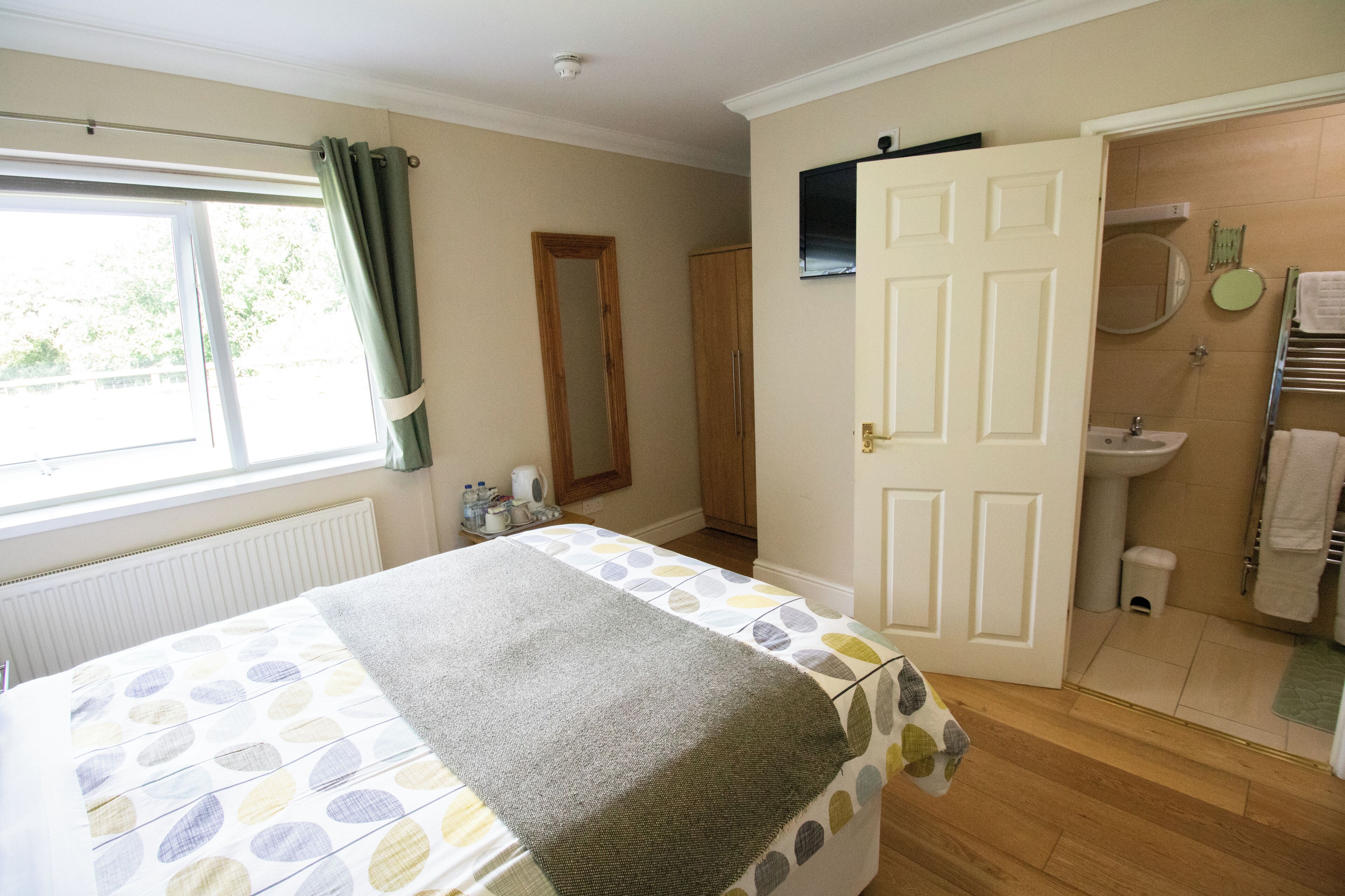 A bedroom with a bed, a window with curtains, a door leading to a bathroom, and a radiator.
