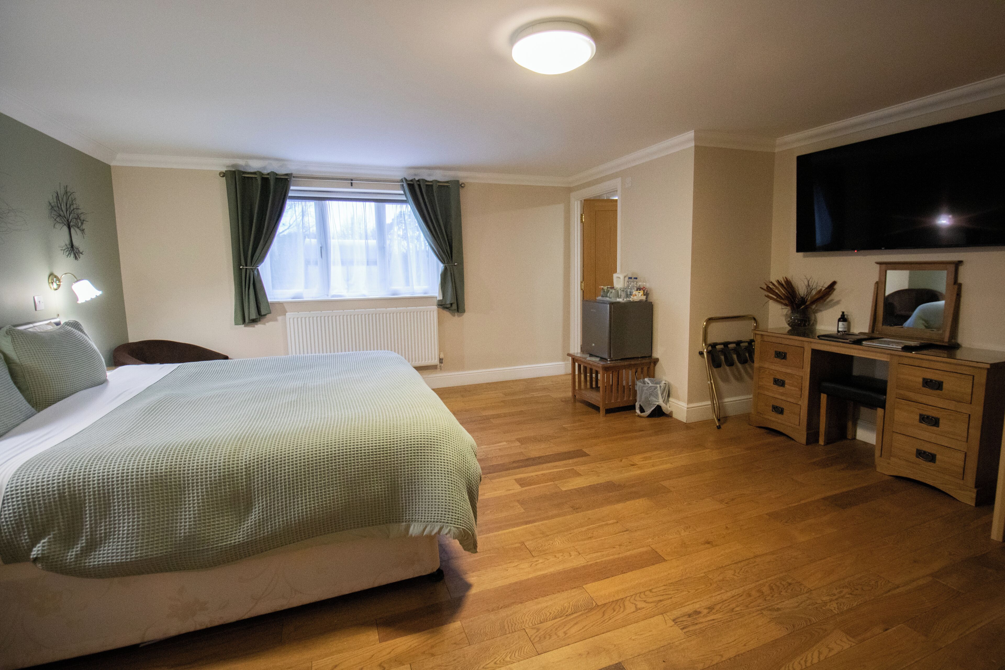 A bedroom with a bed, a desk, a chair, a television, and a radiator.