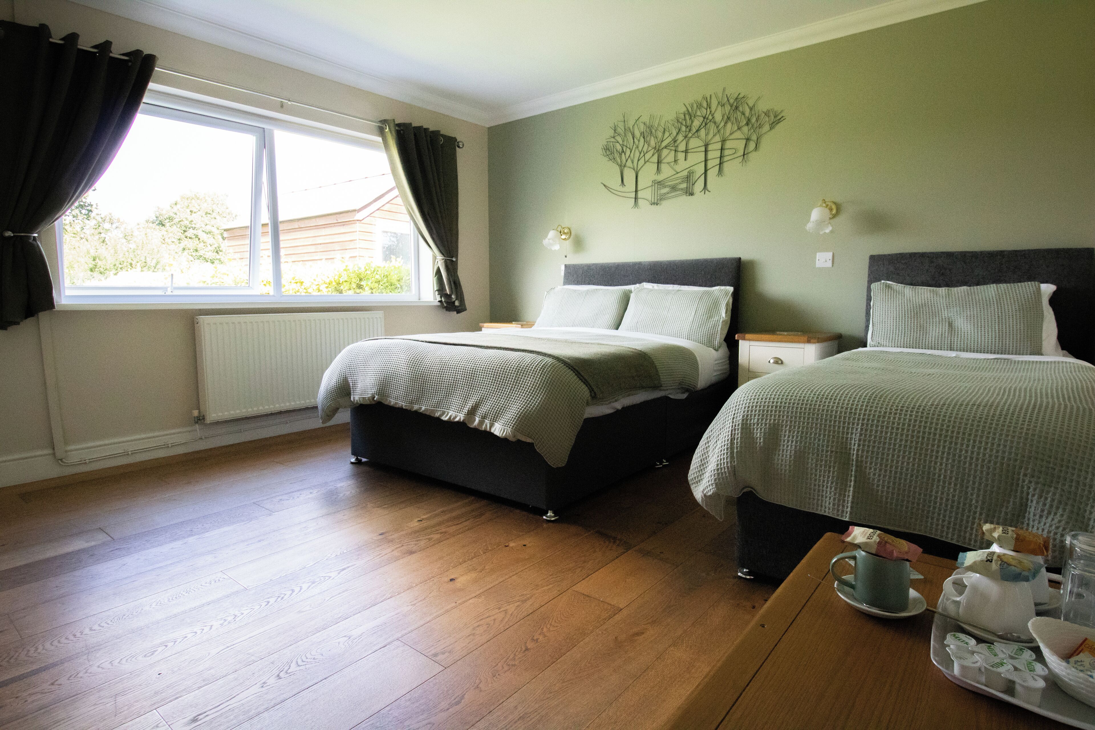 A bedroom with two beds, a wooden floor, a window with curtains, and a wall art piece.
