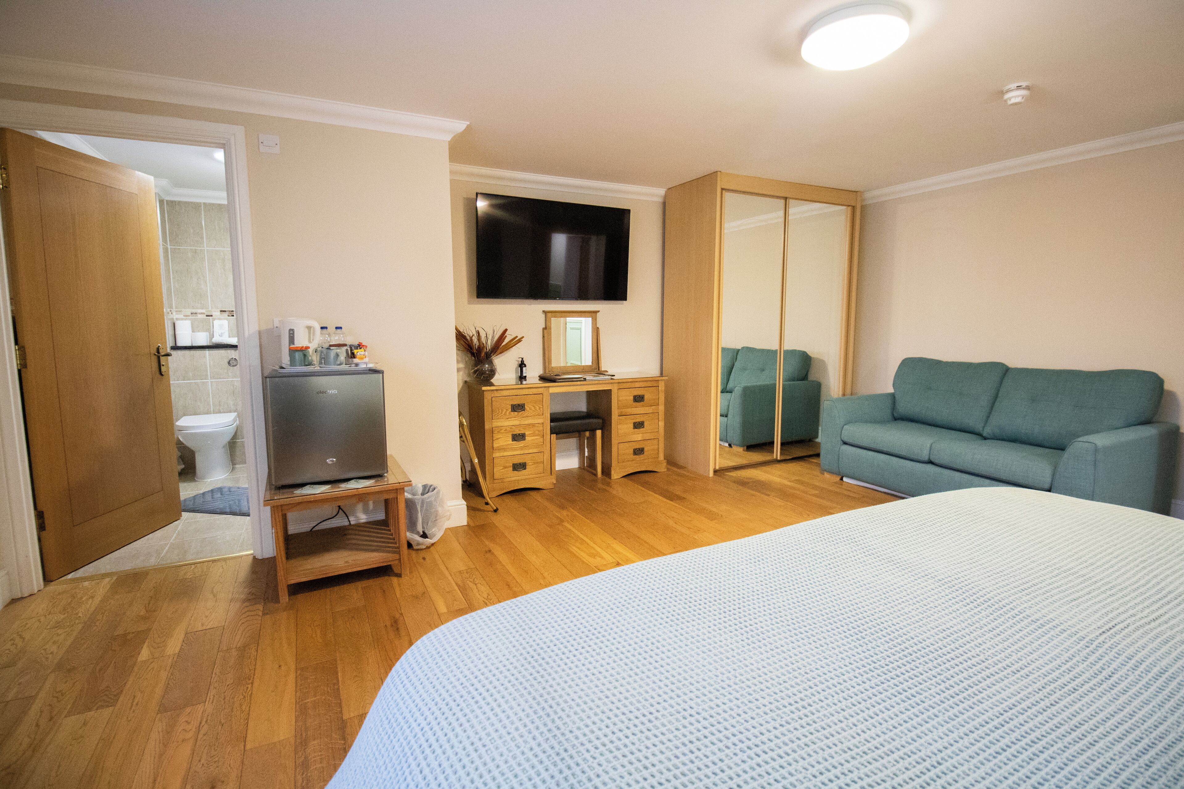 A bedroom with a bed, a TV, a desk, a mirror, and a green sofa.