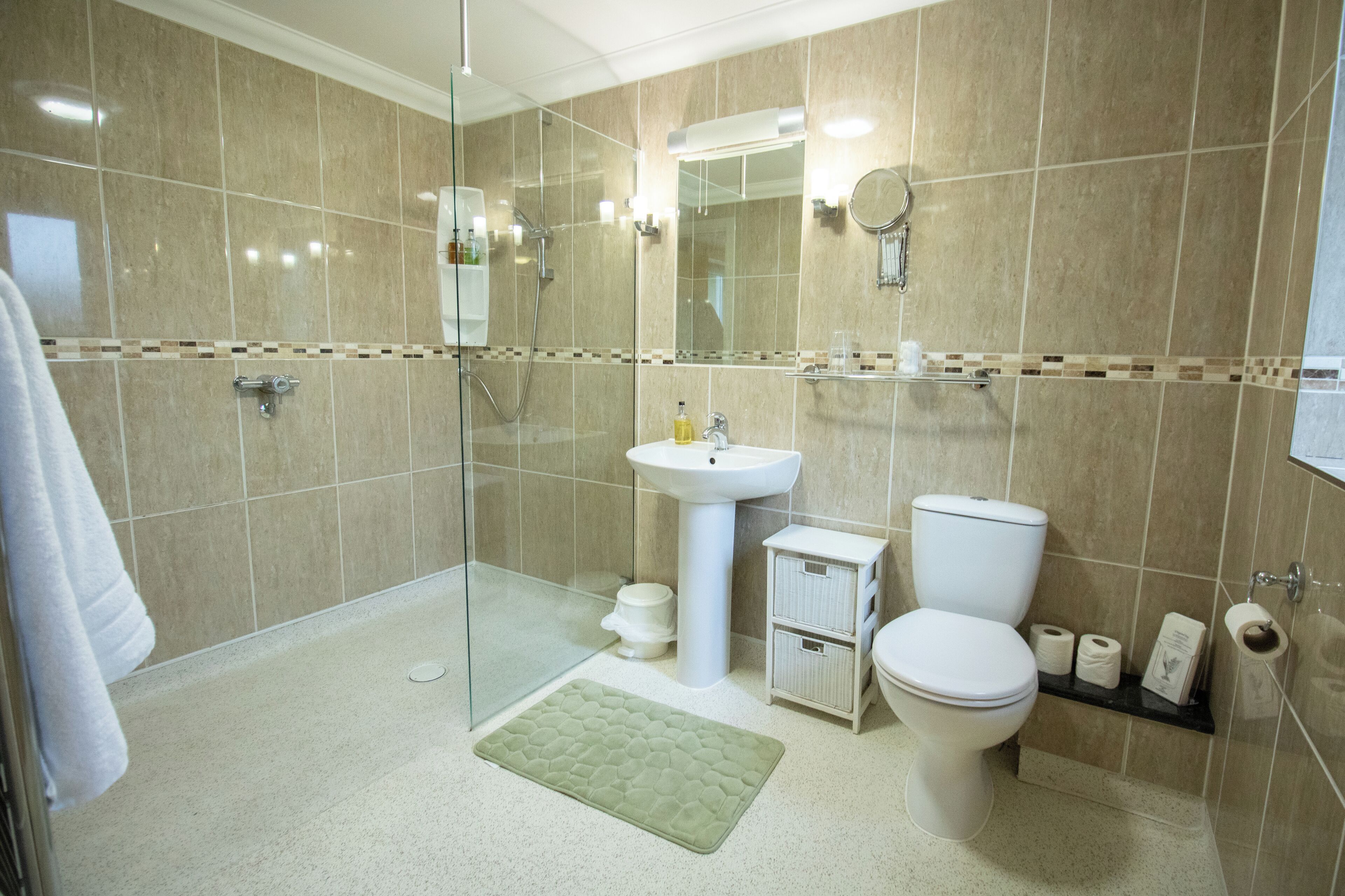 A modern bathroom with a glass shower enclosure, a pedestal sink, a toilet, and a small storage cabinet.