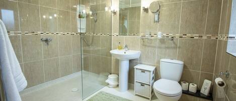 A modern bathroom with a glass shower enclosure, a pedestal sink, a toilet, and a small storage cabinet.