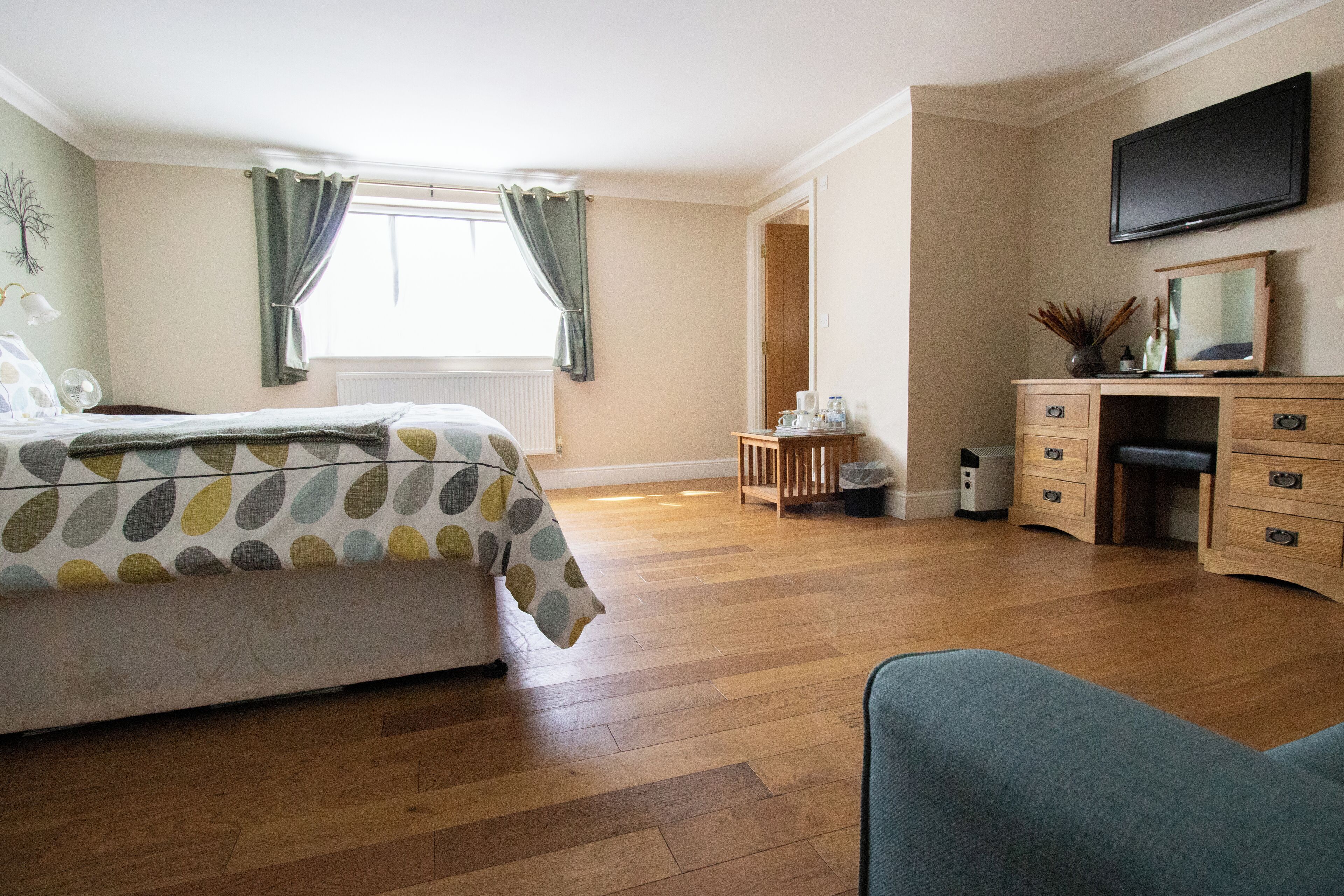 A bedroom with a bed, a desk, a chair, a television, and a window with curtains.