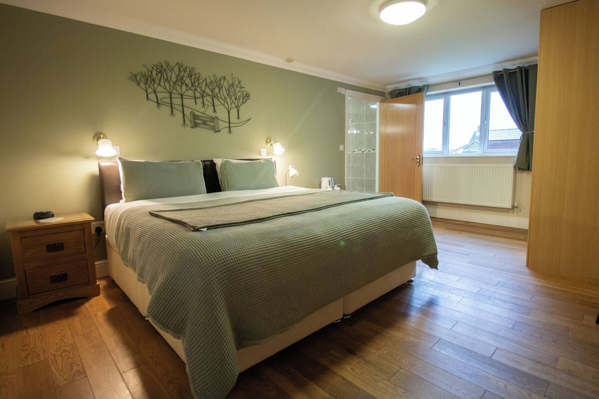 Une chambre à coucher avec un lit, des tables de chevet, des œuvres d’art murales et une fenêtre avec des rideaux.