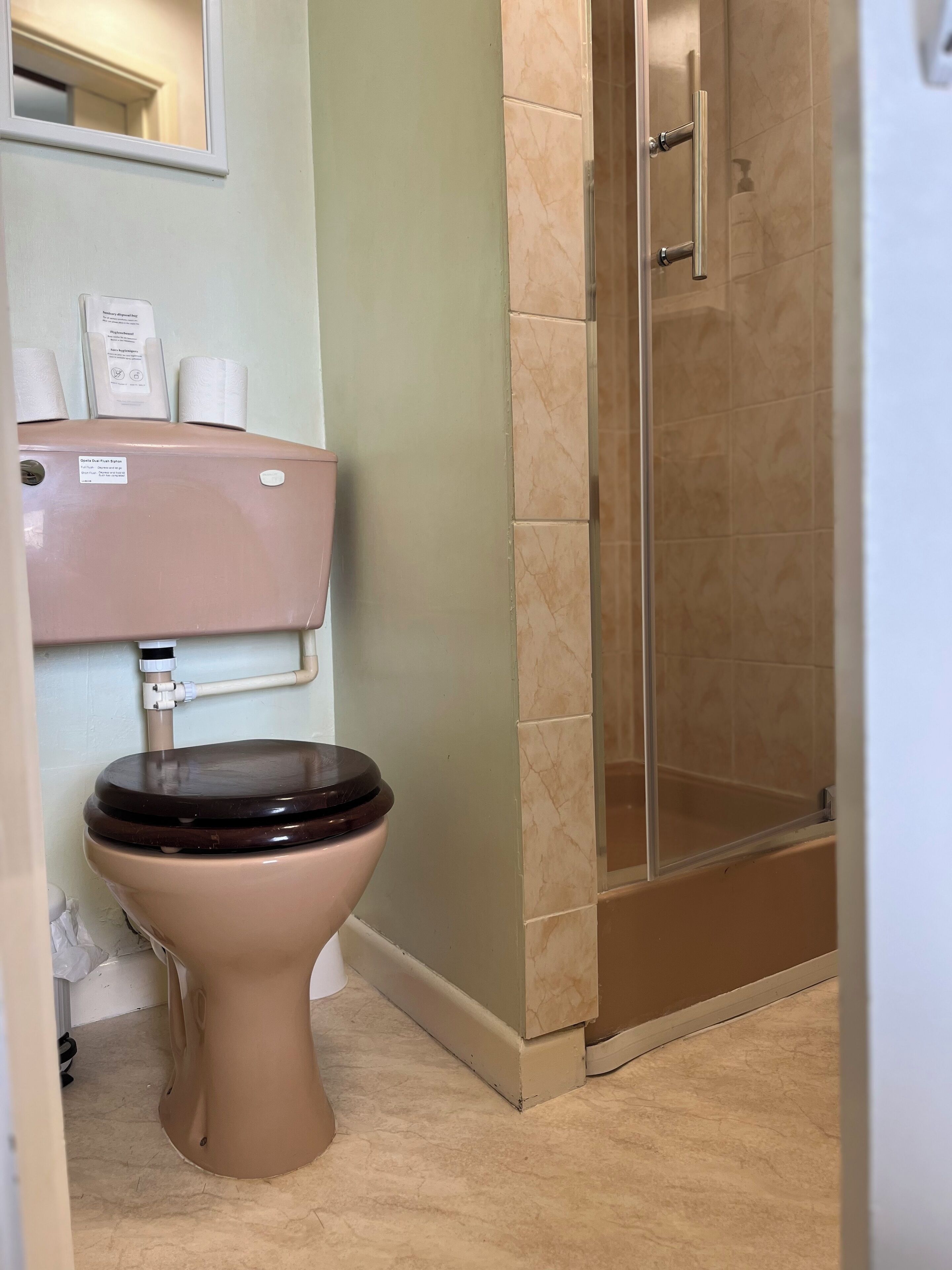 Un baño con inodoro, ducha y espejo.