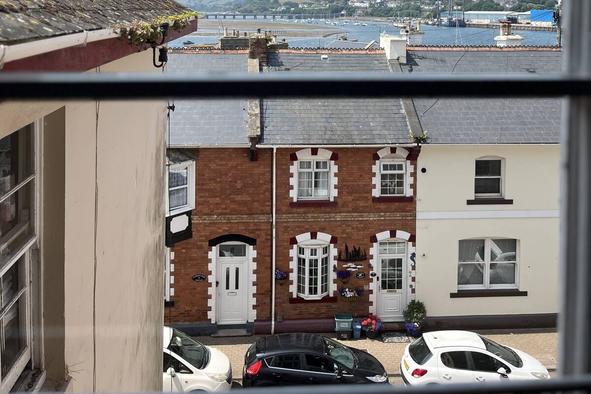 A view from a window overlooking a street with parked cars and a bridge in the distance.
