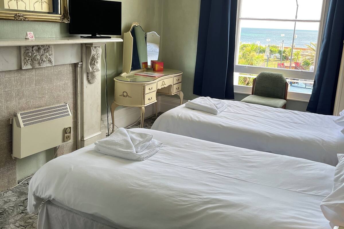 A hotel room with two beds, a vanity with a mirror, a television, and a view of the sea.