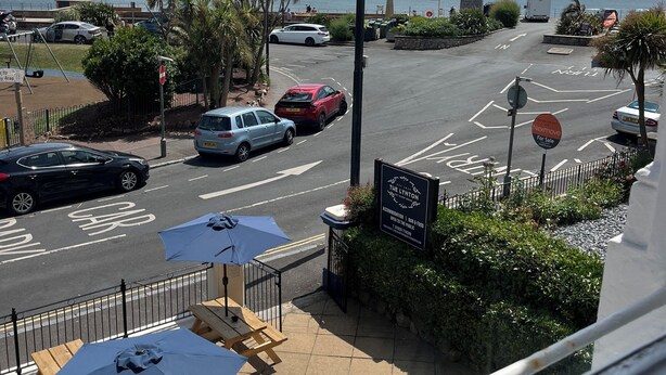 A coastal view with a street, parked cars, and a lighthouse. - Lynton House (Teignmouth)