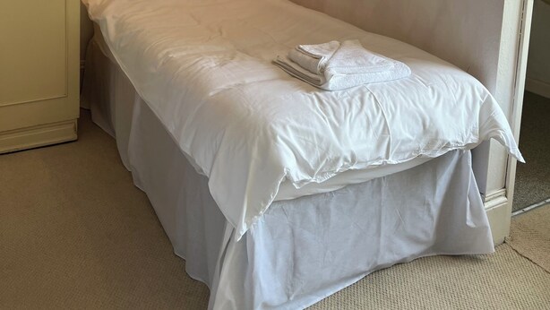 A single bed with white bedding, a hanging lamp, a framed picture on the wall, and a door with a decorative design. - Lynton House (Teignmouth)