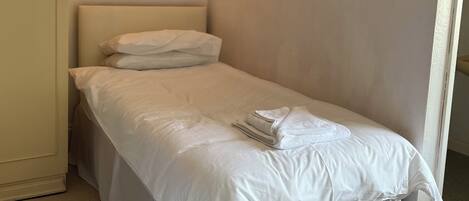 Een enkel bed met witte lakens, een hanglamp, een lijst met een foto aan de muur, en een deur met decoratief ontwerp.