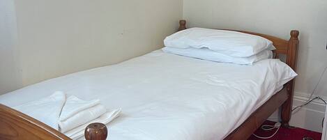 A small, single-bed room with a wooden headboard, white bedding, and a red patterned carpet.