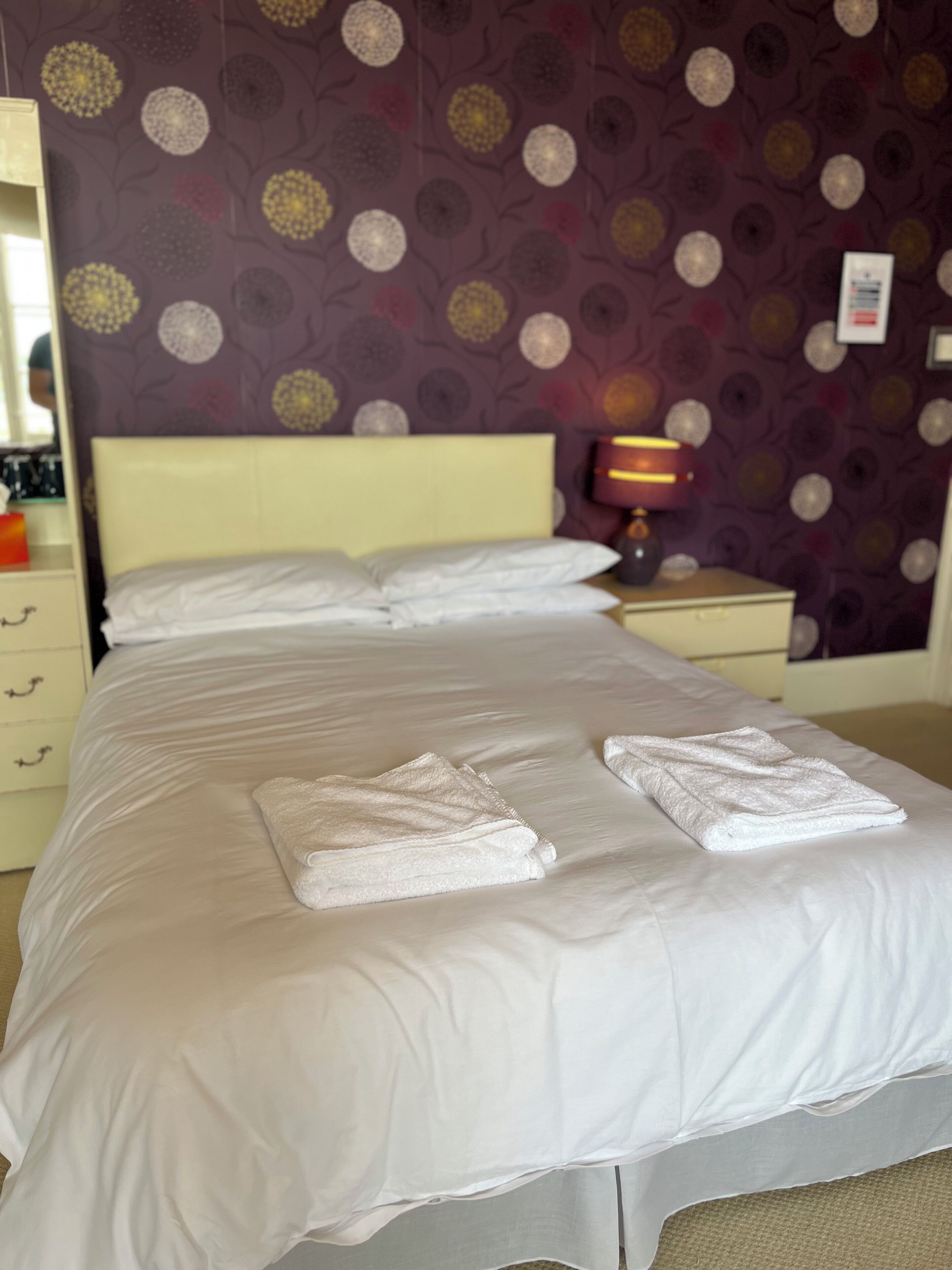 A neatly made bed with white linens and two folded towels on the bed.