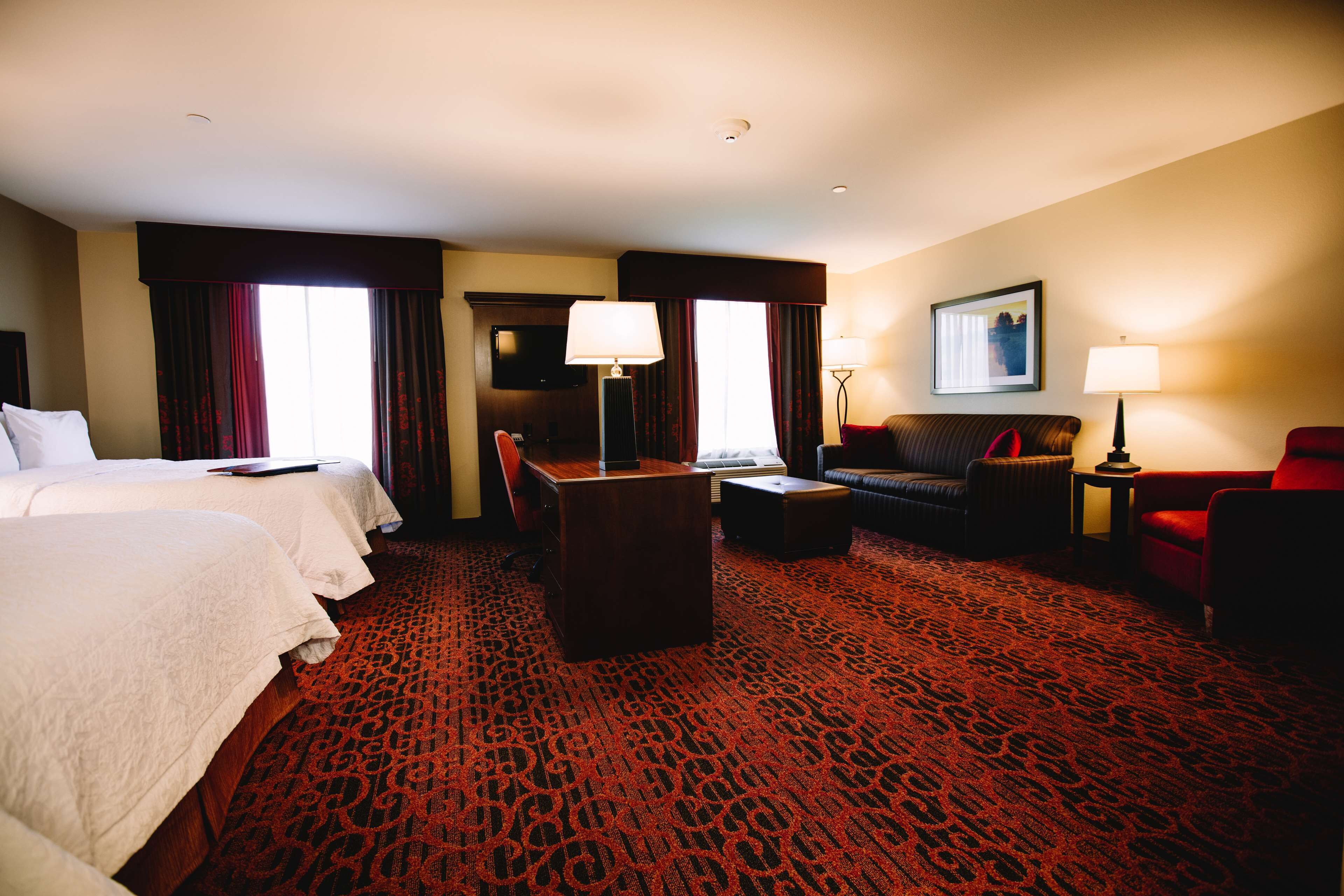 A hotel room with two beds, a desk, a sofa, and a red carpet.