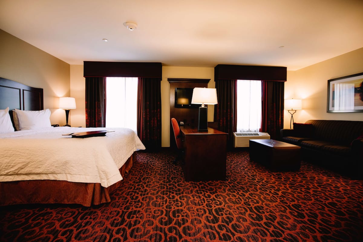 A hotel room with a large bed, a desk, a chair, a sofa, and two lamps.