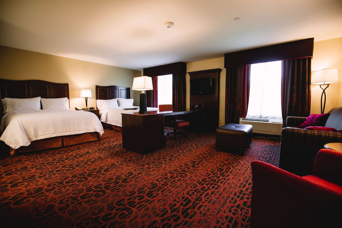 A hotel room with two beds, a desk, a chair, a sofa, and a TV.