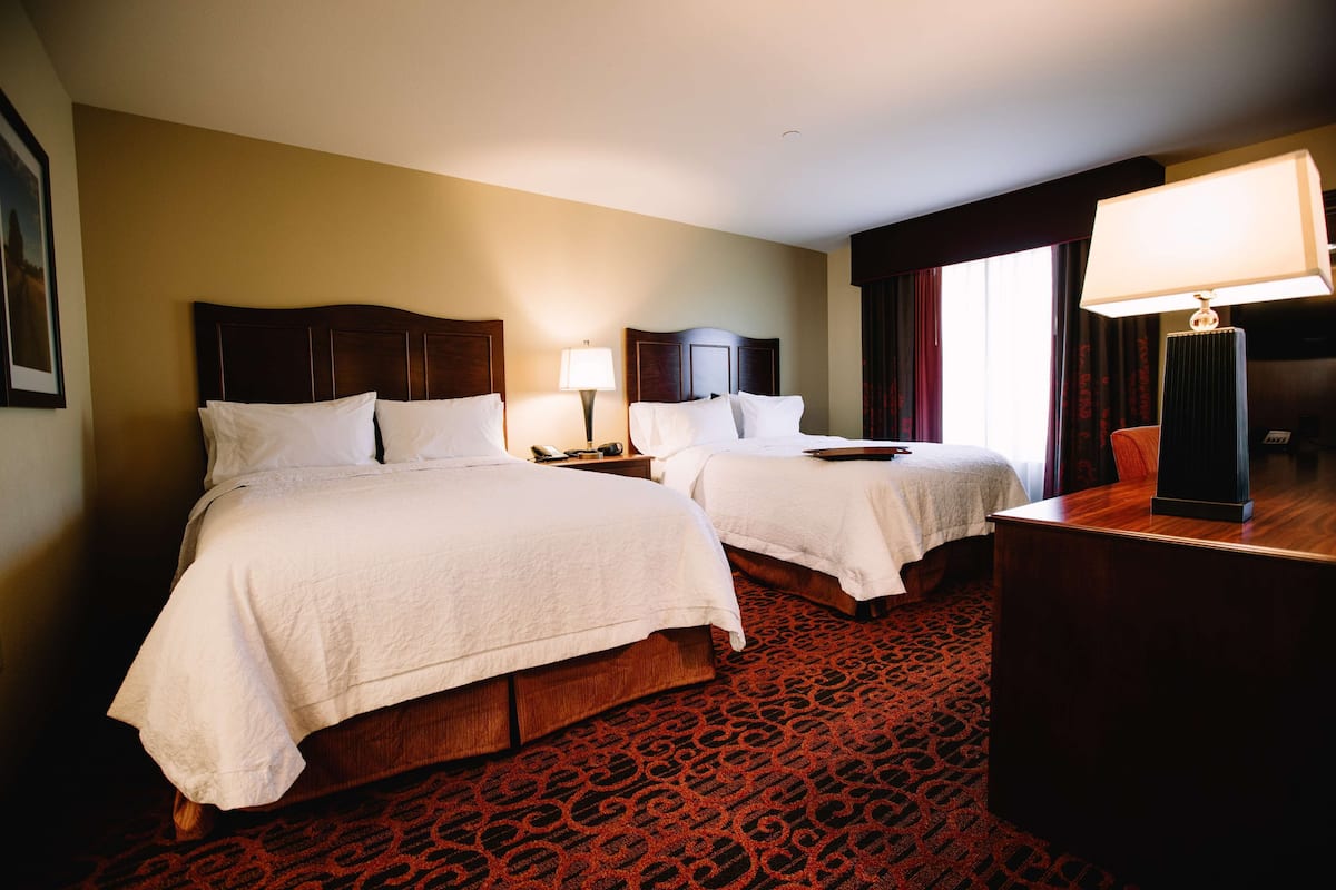A hotel room with two beds, a desk, a lamp, and a patterned carpet.