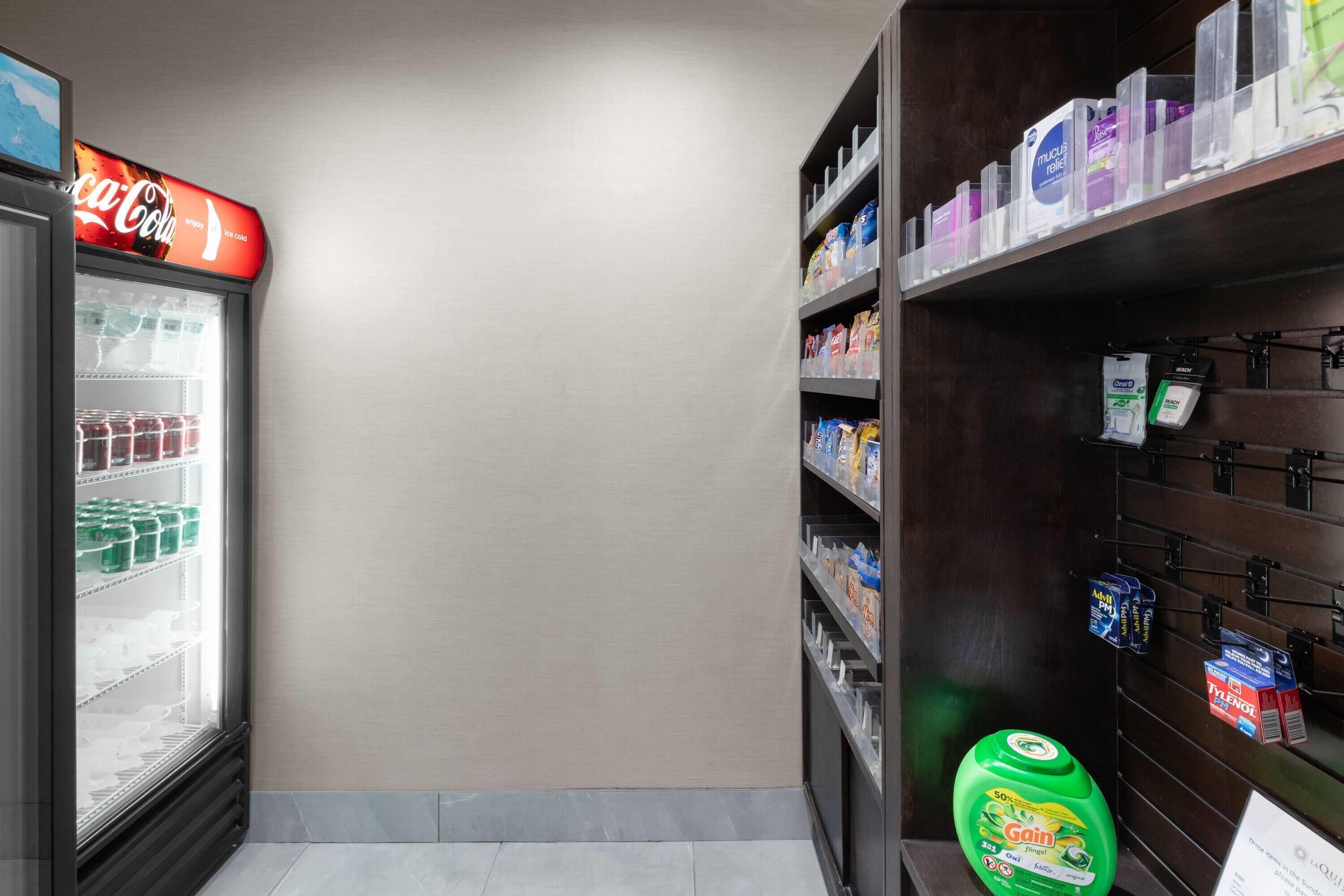 A vending machine with a Coca-Cola sign, a refrigerator stocked with drinks, and shelves with various products including cleaning supplies.