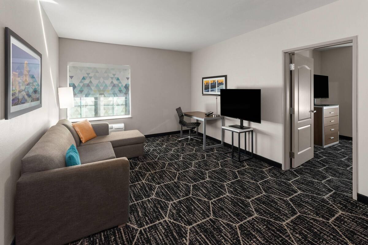 Habitación de hotel con sofá, televisión, escritorio y puerta que da a un baño.